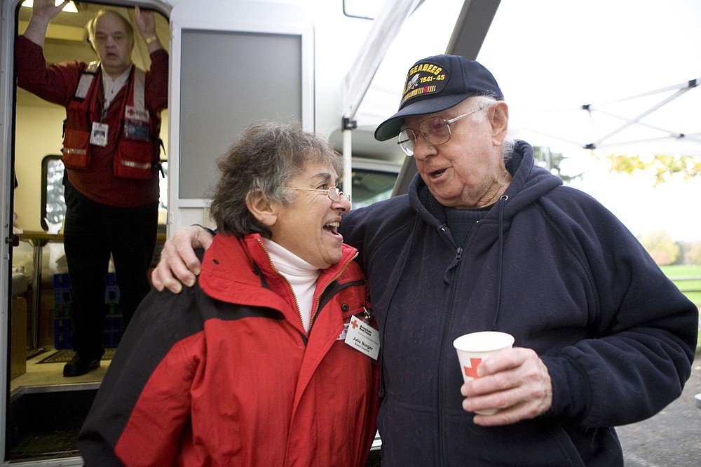 Vivian Johnson/ for The Columbian
Julie Burger sings and old Navy song with Norm Kime, who served as a Navy SeaBee during World War II, as Burger joined other Red Cross volunteers to give away coffee and doughnuts Saturday to veterans at the 23rd annual Celebrate Freedom Veterans Parade at the Fort Vancouver National Historic Site.