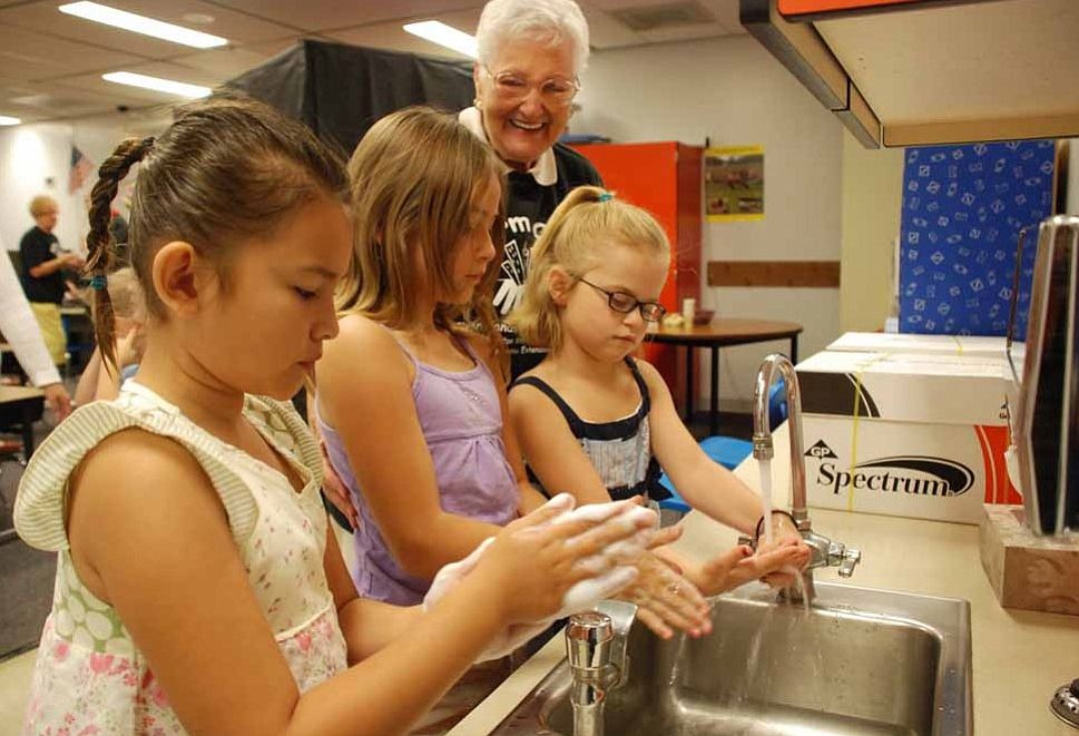 Hearthwood: Hearthwood Elementary School students Alyssa Dolan, from left, Lydia Poss and Jaci Raugust, along with a volunteer from the Columbia Crest Lions Club, practice washing their hands properly as part of a Germ City traveling display that has visited several schools this flu season.