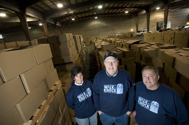 Photos by STEVEN LANE/The Columbian
Walk &amp; Knock leaders, from left, Susie Rawson, Joe Pauletto and Dave Rawson take a break in front of 8,900 boxes of donated food.