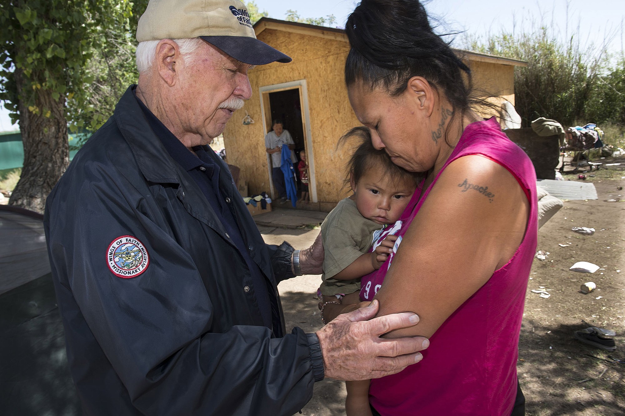 Dale Whinery says for a prayer for Carol Hinton and her family as she holds her daughter Lettie, 2, at her home in San Carlos Apache Reservation in Arizona.