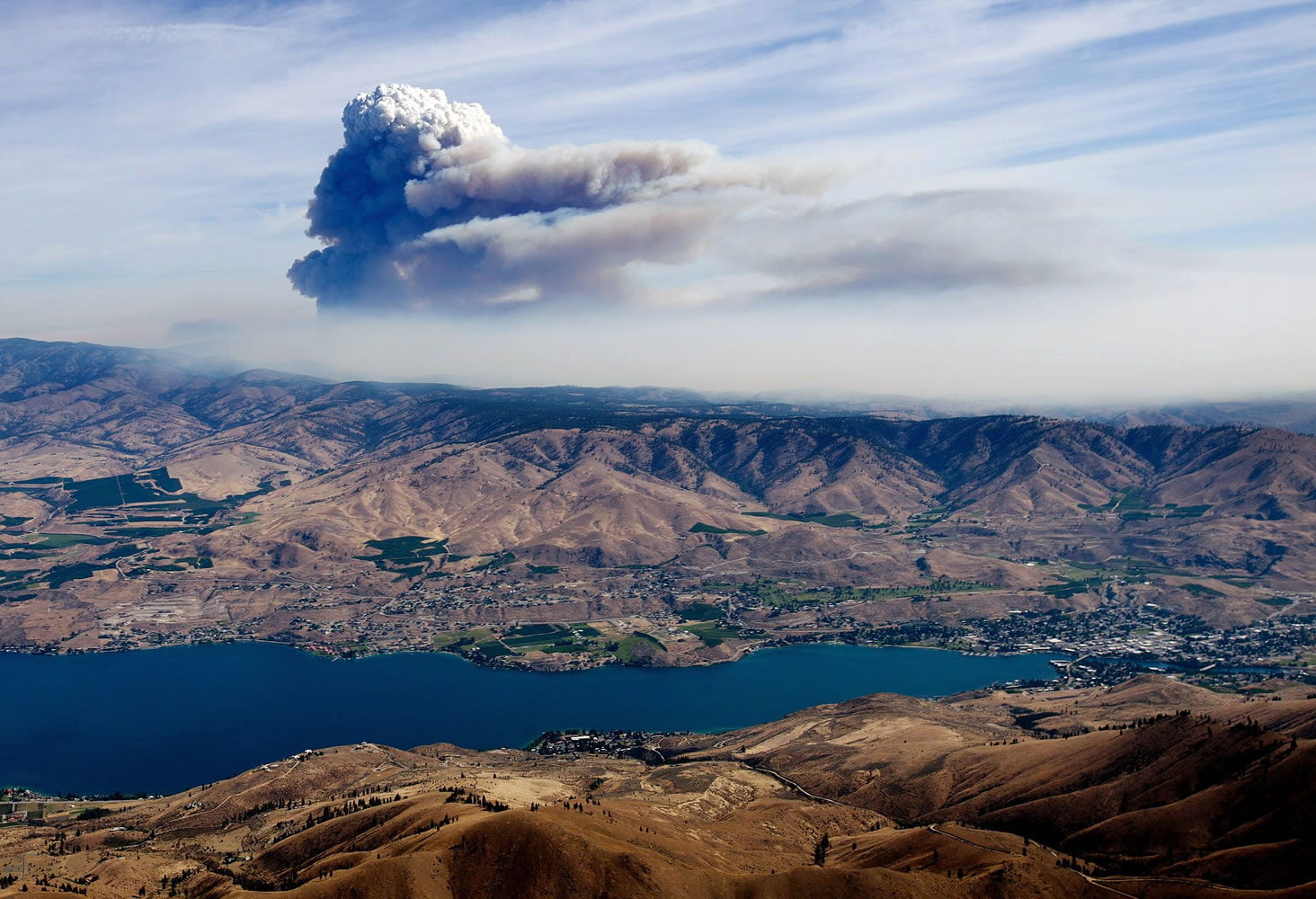 With Lake Chelan. in the foreground, a large plume of smoke and steam rises from behind the ridge, just south of Pateros on July 18, 2014, from the Carlton Complex Fire.