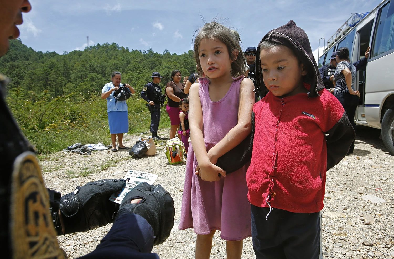A little girl clutches her brother's hand as she answers simple questions about her name and those of her parents on July 4 in Ocotepeque, Honduras. Miguel Martinez Madrid, left, who leads a special police unit trying to slow the flow of migrants, holds the siblings' Honduran ID cards. Questions are designed to find out if the children are being smuggled to the United Stats.