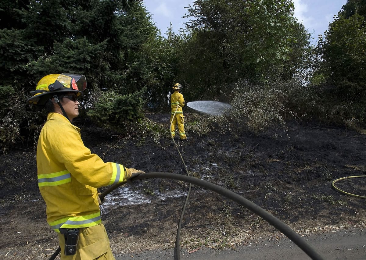 Vancouver firefighters Jae Munson, left, and Travis Meyers put water on hot spots after a grass fire along Interstate 5 in August 2011. Despite recent rain, there's still fire danger, officials say, and a burn ban remains in effect.