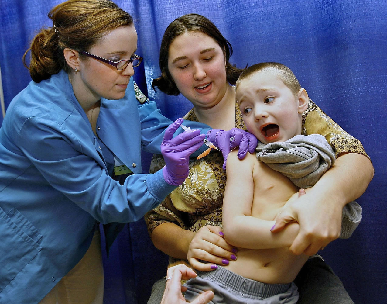 Anton Sheperd, 4, attempts a quick escape while his mother Tiffany Adkins holds him and nursing student Tiffany Stacy administers a shot at a February 2009 immunization clinic in Roseburg, Ore.