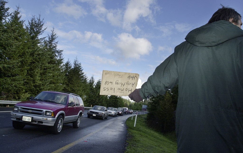 A man panhandles along a highway offramp in Vancouver.