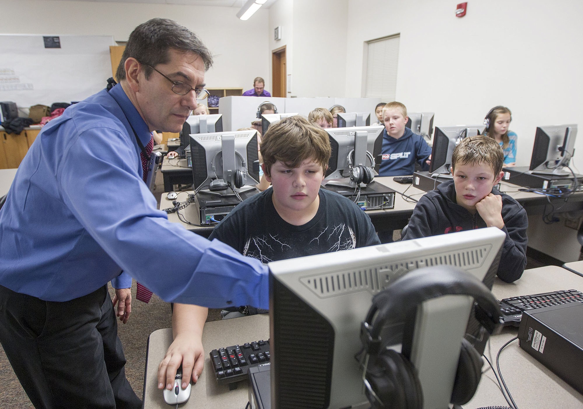Frederick Tillman, computer teacher at Amboy Middle School, left, helps sixth-grader Ely Earl, center, in an Hour of Code puzzle.