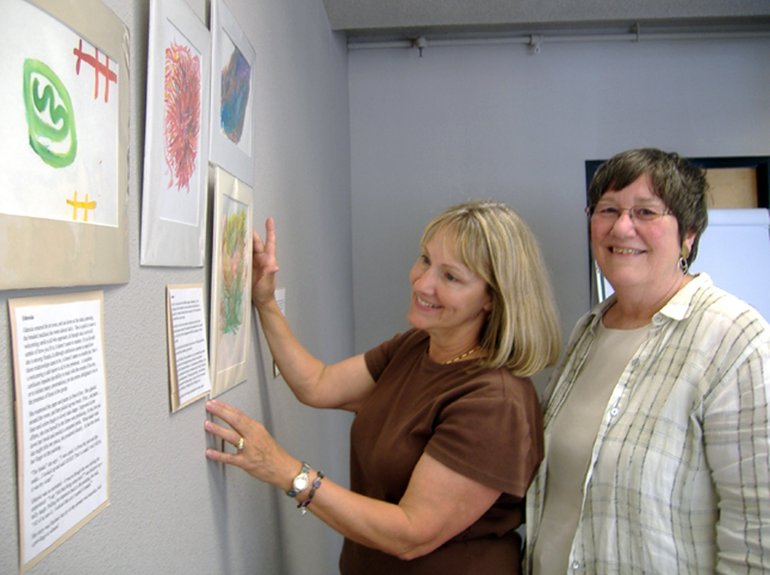 Pat La Croix, left, and Marti Sanders hang a display of art created by adults suffering from dementia at the Greater Vancouver Chamber of Commerce.