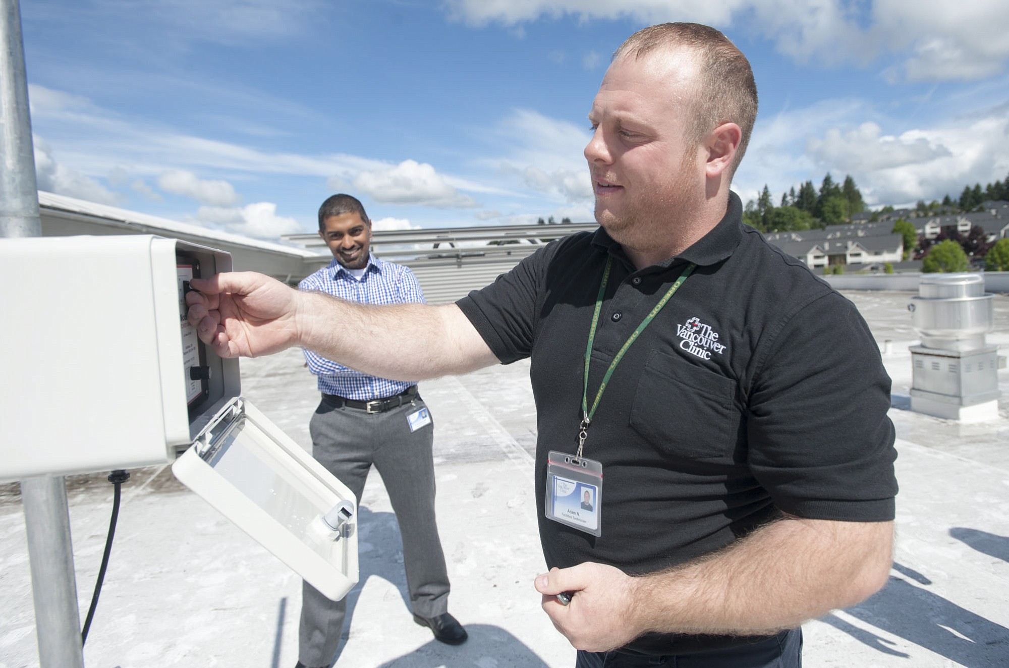 Facilities technician Adam Norman tests the pollen counting machine on the roof of The Vancouver Clinic Salmon Creek office as Dr. Raj Srinivasan looks on. Norman collects samples from the roof three days a week.