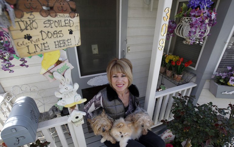 Tammy Kassis sits with her dogs, Chelsea, Coco-Puff and Darla, in front of their 11-foot tall Victorian doggie mansion in Winchester, Calif.