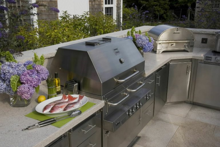 This outdoor kitchen features a stainless-steel grill, pizza oven and cabinets that are easy to maintain.