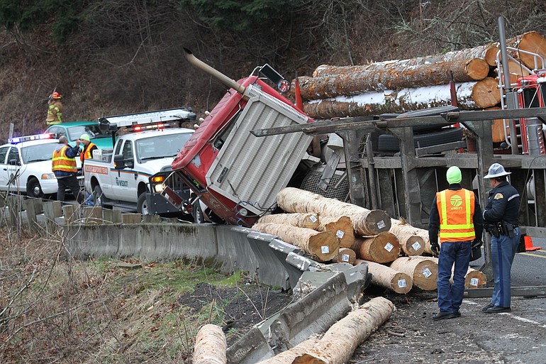 Officials deal with a loaded log truck that rolled over on state Highway 14 about 2 p.m.