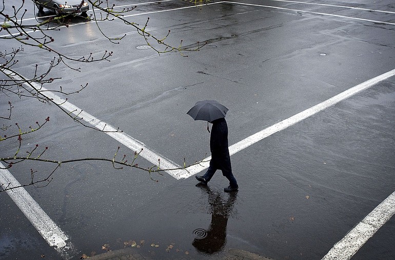 A pedestrian shields himself against the rain while crossing a street in downtown Vancouver.