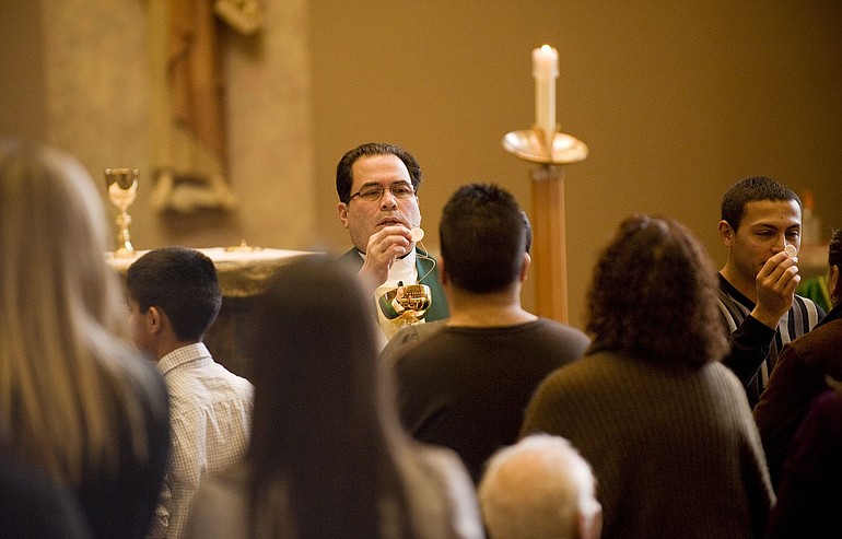 Father Armando Perez gives communion during a Spanish-language mass at St. John the Evangelist Catholic Church on Sunday.