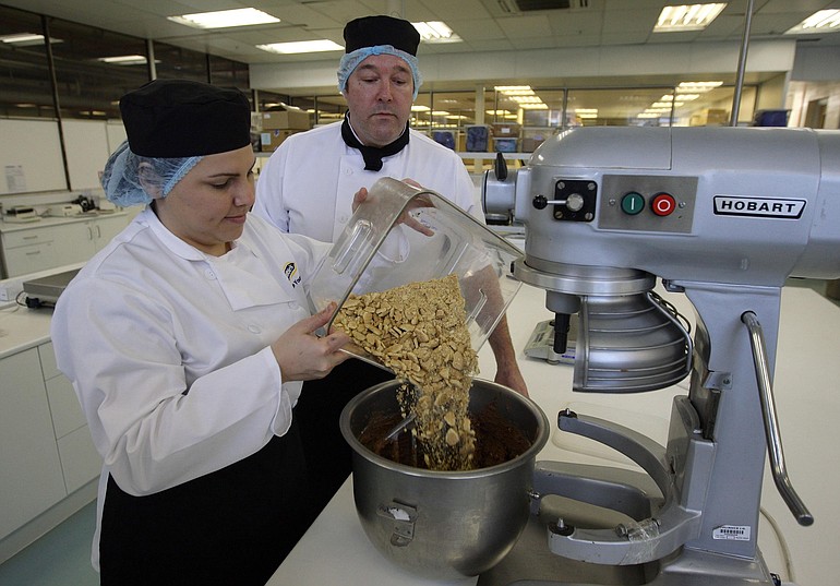 Cake Design and Development Head Chef Paul Courtney, right, and Product development Technologist Katie Young pour biscuits into a cake mix as they practice making a biscuit cake at a biscuit factory in Stockport, England.