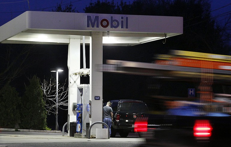 A man pumps gas as a truck whizzes by a Mobil Station in Stoneham, Mass. Tuesday. Exxon Mobil Corp.