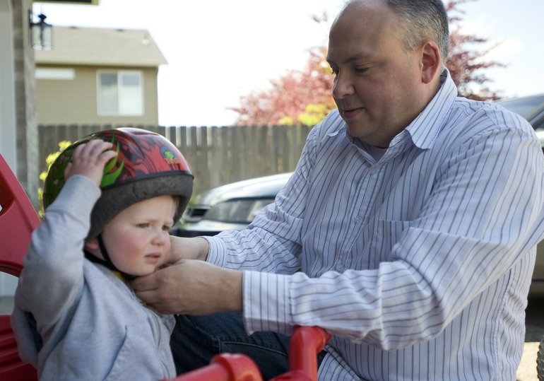 Jerry Gowen earned his MBA degree this year after four years of night classes at Washington State University Vancouver. Here, he straps a helmet on his son, Scott, 20 months old, outside his Felida home.