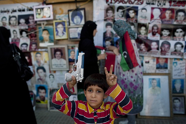 A boy holding a plastic weapon poses for a picture Monday in front of portraits of people who were killed or have disappeared during Moammar Gadhafi's regime in Benghazi, Libya.