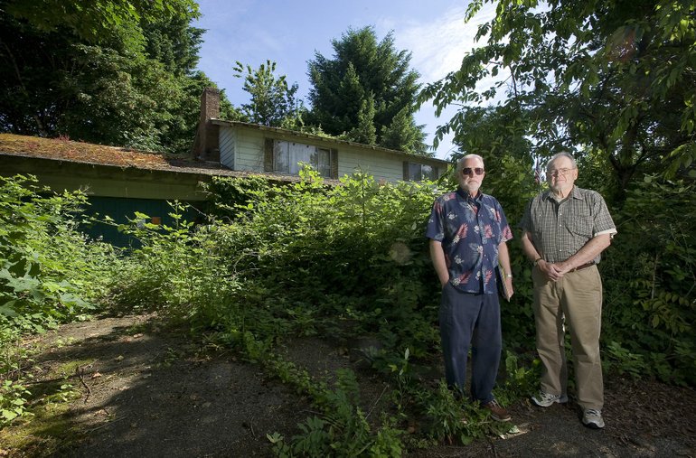 Concerned neighbors Jim Faull, left, and Ed McMillan stand in front of an abandoned home that they say is a haven for critters and an eyesore. The city says it lacks the money to do much for most junky houses.