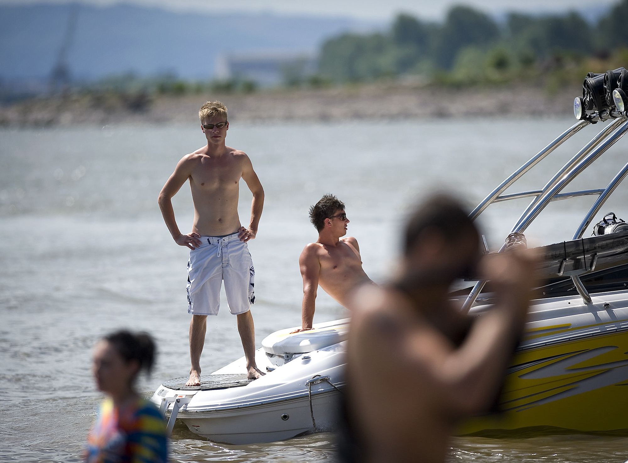 Russ Terekhov, center left, 22, looks along the beach from the stern of his ski boat while he and his friend Rod Nekrasov, 21, wait for more friends before going wakeboarding Sunday at Wintler Park.