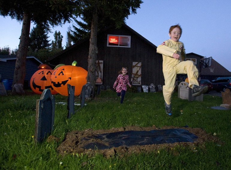 Max Milton, 9, leaps over a decorative grave in the front yard of his home as Mikah Brandt, 6, pursues him.