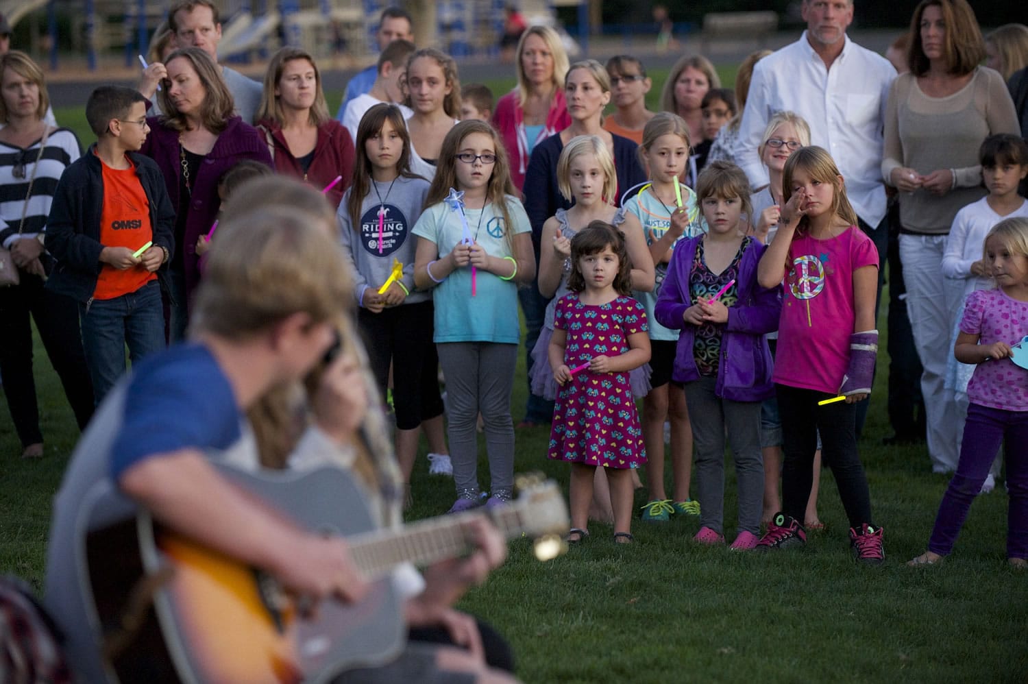 Photos by Steven Lane/The Columbian
Classmates, teachers and friends listen to a rendition of Ben Harper's song &quot;Waiting on an Angel&quot; on Wednesday evening at a vigil for Stormy Solis at Fisher's Basin Community Park in east Vancouver. The 7-year-old girl died from a brain injury after reportedly falling off a swing at Fisher's Landing Elementary School.  At top, a picture of Stormy on display at the vigil.