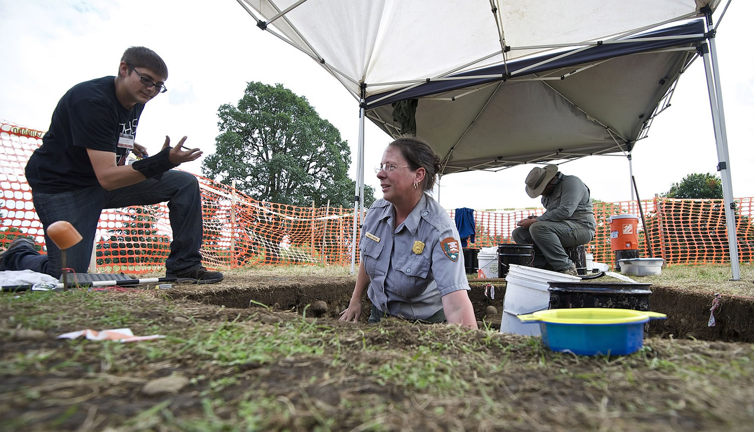 Portland State University student Tyler Molter, from left, takes an artifact Tuesday from National Park Service archeologist Beth Horton during excavation of a flag pole site on the Parade Ground at Vancouver Barracks.