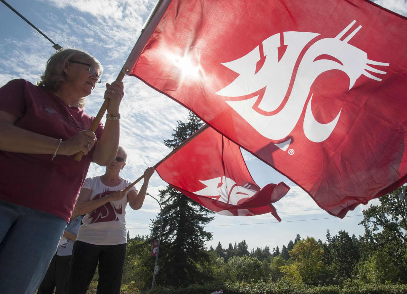 Jan Johnson, left and Joan Dengerink welcome students by waving crimson cougar flags on the first day of classes at Washington State University Vancouver on Monday. Johnson was the assistant to Hal Dengerink, founding chancellor. Joan Dengerink is his widow.