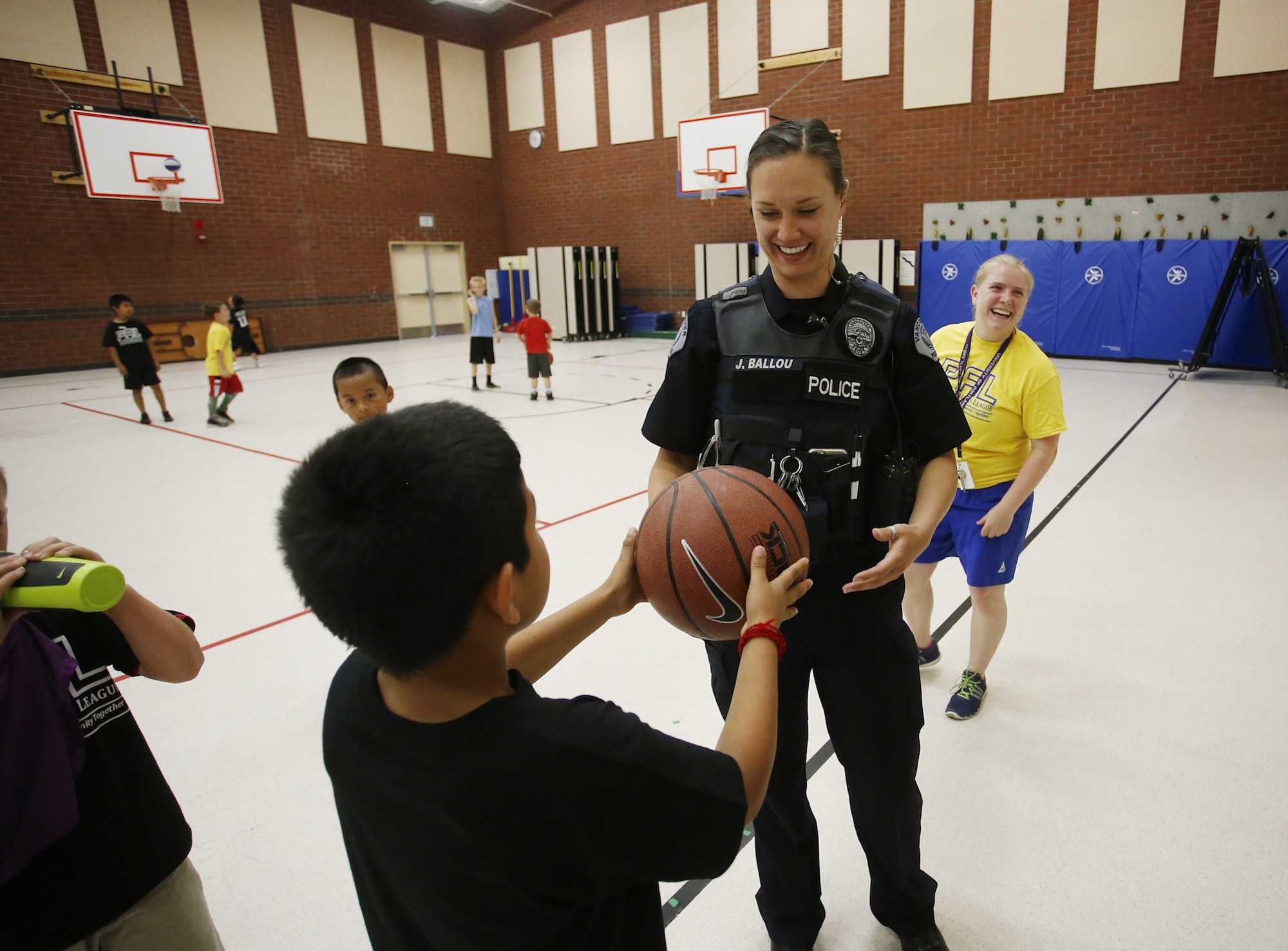 Photos by Steve Dipaola for the Columbian
Vancouver police Officer Julie Ballou accepts a basketball from a boy at Police Activities League of Vancouver summer camp at Orchards Elementary. Jenny Thompson, right, in yellow shirt, executive director of PAL, served as referee.