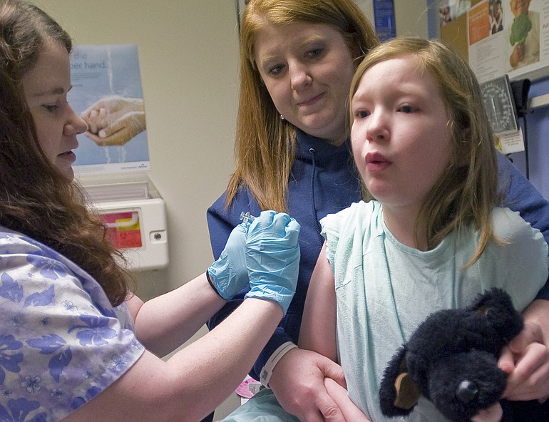 Barbie Allmaras, of Heisson, holds her daughter Ellen, 7, as medical assistant Jenny Gager injects her with a flu vaccination at Kaiser Permanente's Salmon Creek campus on Thursday.