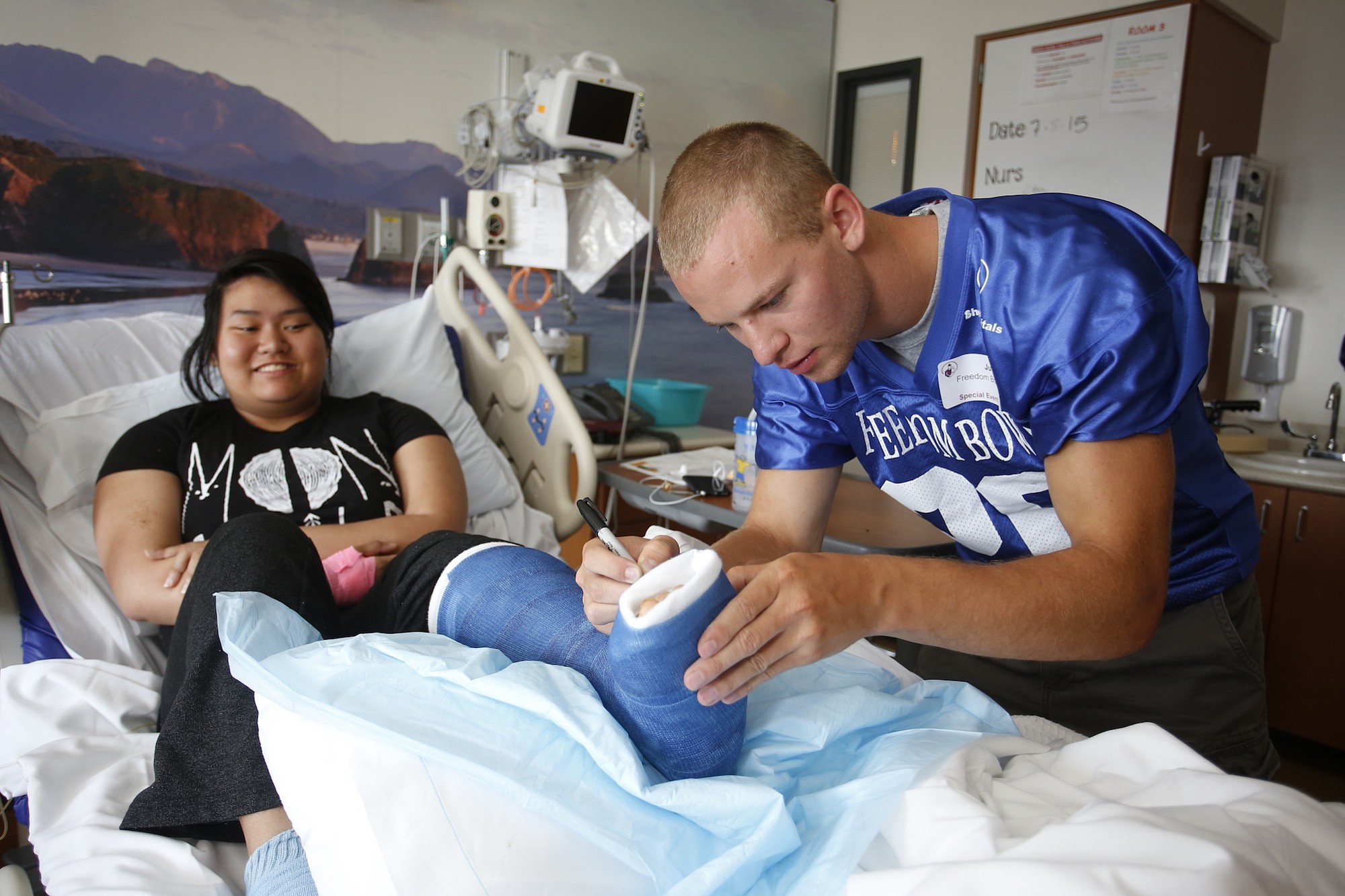 Freedom Bowl Classic football players visiting children in the hospital. Tucker Anderson of Hockinson signs cast for patient Chloe Ouchida, of Portland, age 16.