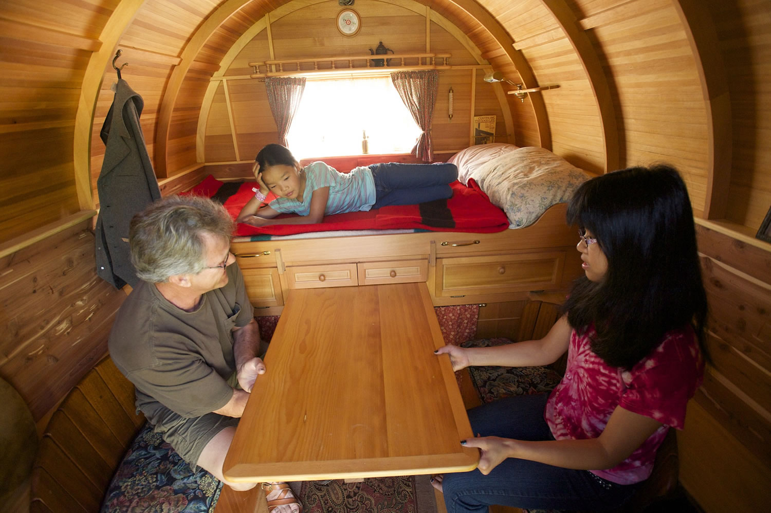 Photos by Steven Lane/The Columbian
Mick Robins sits at the pull-out table of his camper with his daughter, Pei, 15, while daughter Sadie, 11, rests on the bed.