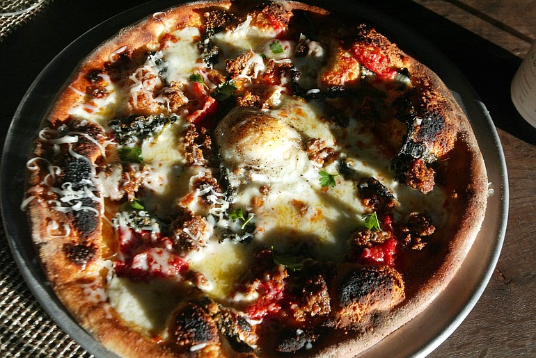 A sunny-side-up egg is one of the ingredients to pizza topped with garlic, roasted tomatoes, kale greens, mozzarella and Parmesan cheese at Hudson restaurant in Oakland, Calif.