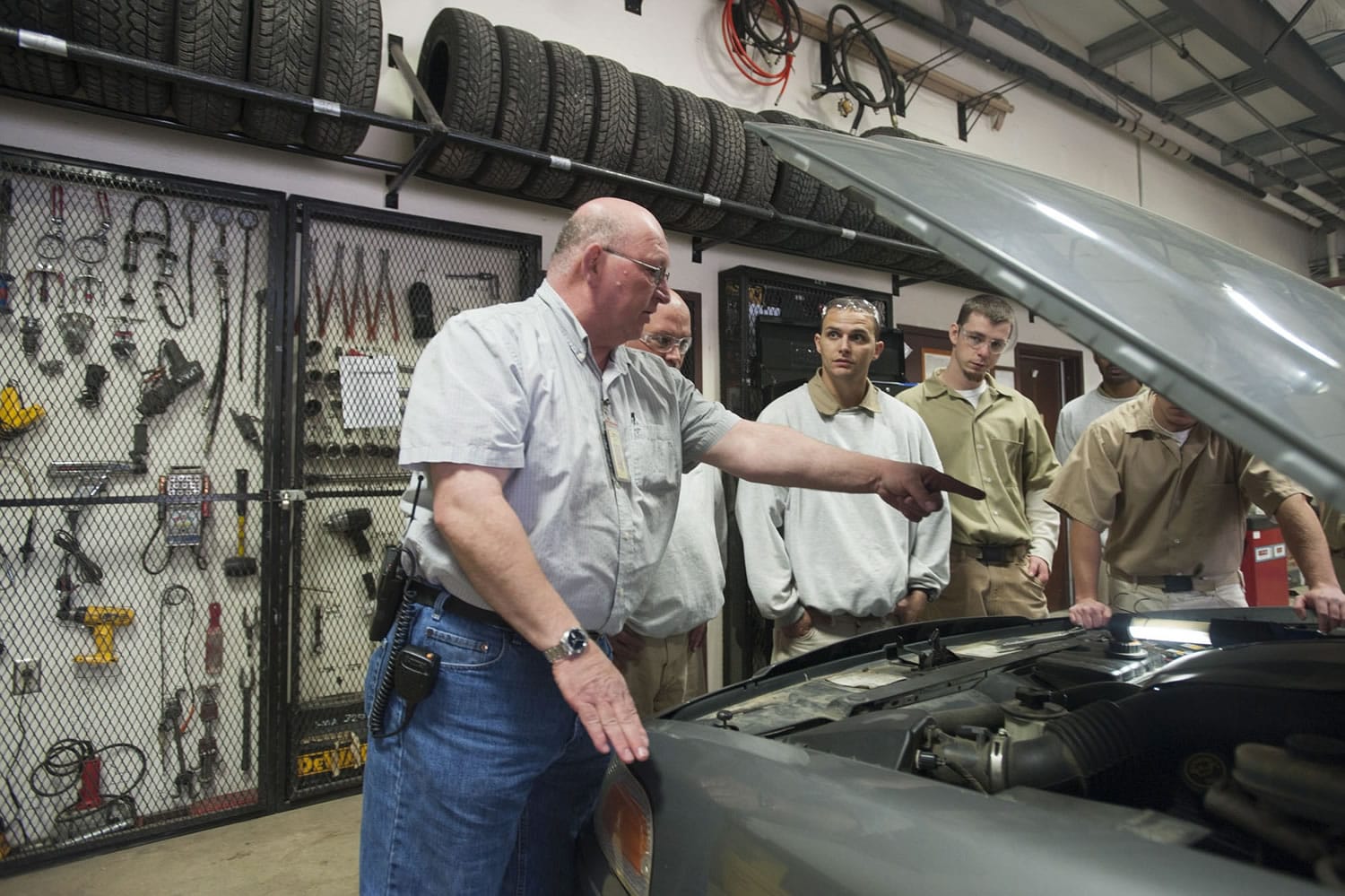 Clark College instructor Bruce Music, left, teaches offenders about changing belts in an automotive repair class at Larch Corrections Center.