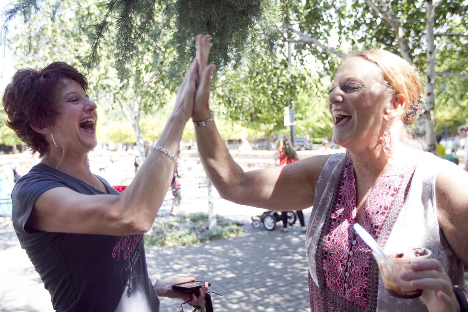 Susan Pagel of Battle Ground, left, high-fives fellow breast cancer survivor Becky Ewer at a social event sponsored by the nonprofit Pink Lemonade Project this summer in Jamison Square in Portland.