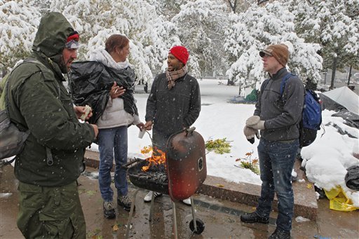 Wall Street protesters huddle around the fire in a BBQ grill to keep warm in City Park in Denver on Wednesday, Oct. 26, 2011. A winter storm moved through the area bringing snow and freezing temperatures.