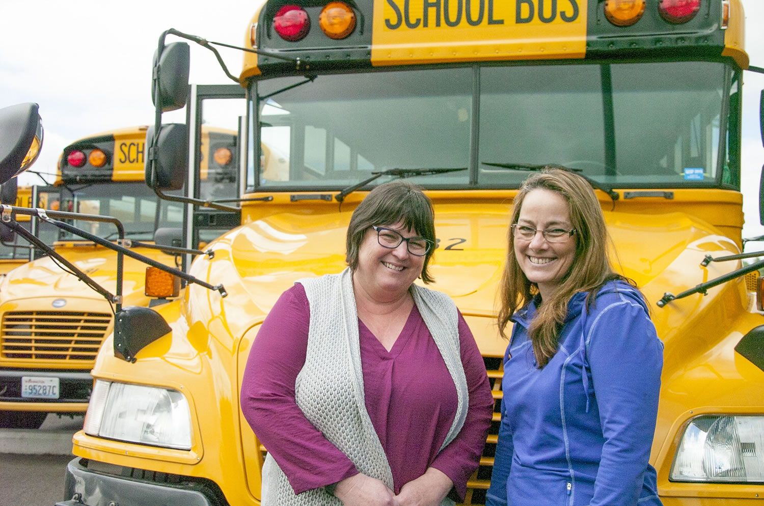 Judit Prihoda, left, and Ileen Neibert, right, pose for a photo in front of Neibert's bus at the Camas School District's transportation headquarters.