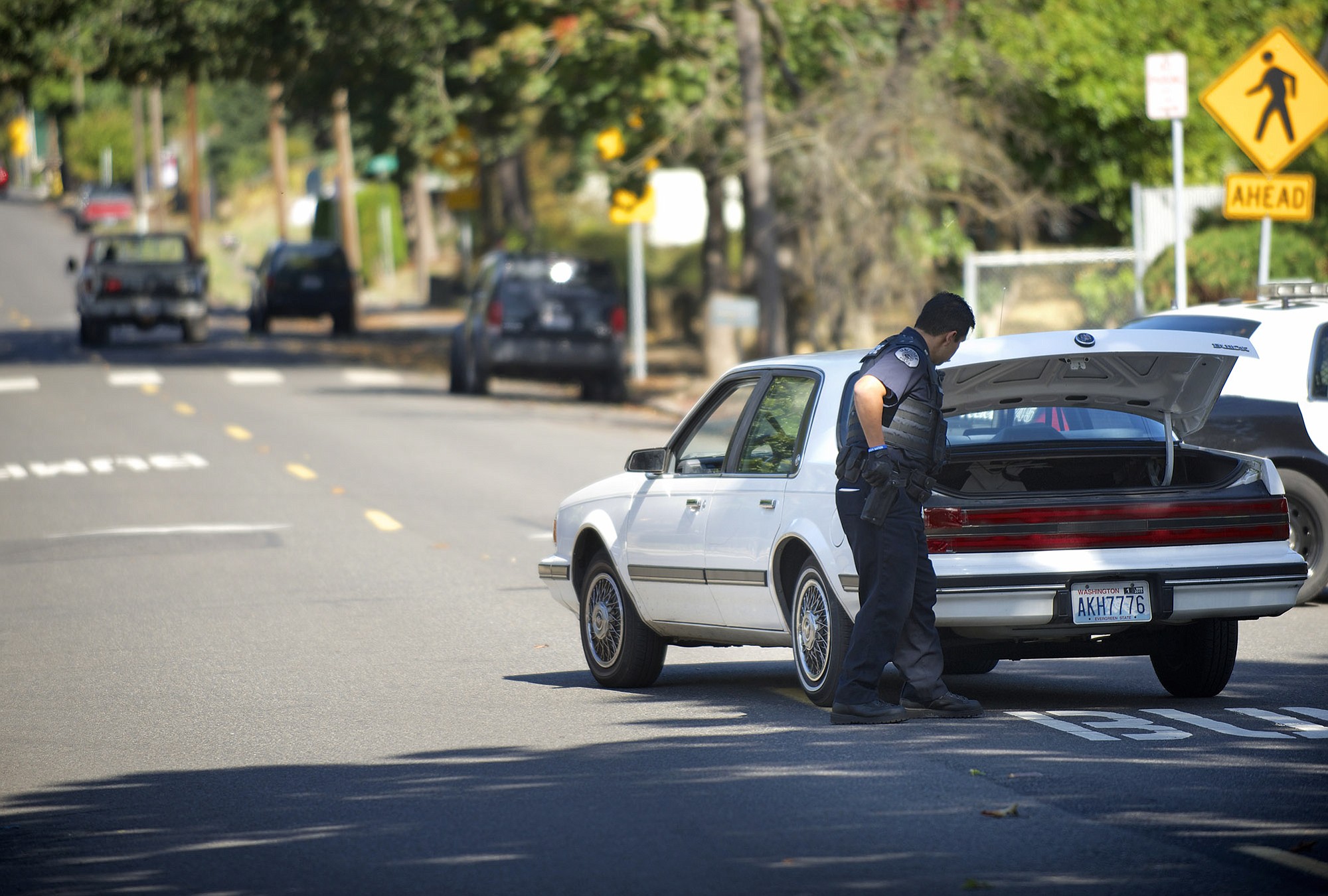 A Vancouver Police officer searches the trunk of a passing car for a suspect in a fatal stabbing on Kauffman Avenue on Thursday.