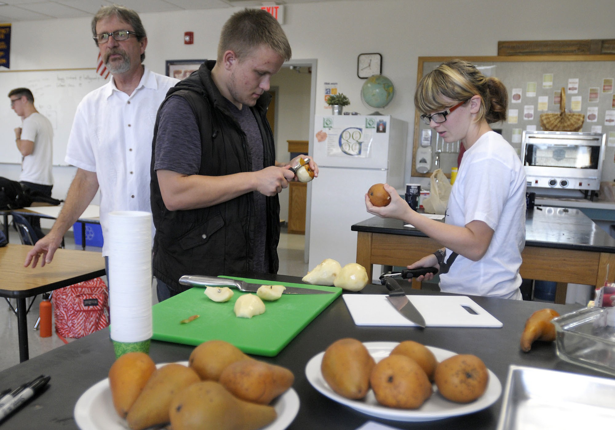 CASEE students Jeramiah Young, in black vest, and MacKenzie Graham peel bosc pears grown in CASEE's orchard.