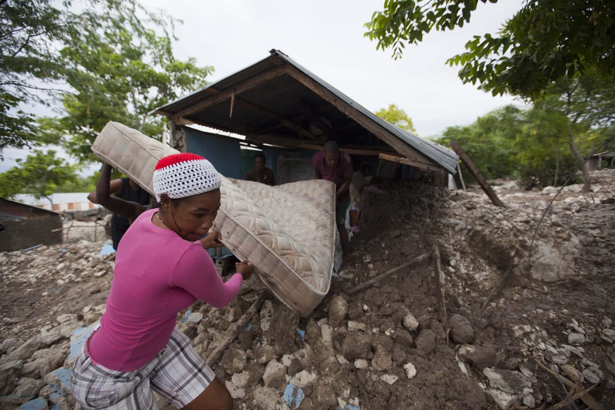 Residents salvage a mattress from a home partially submerged in mud from a mudslide triggered by Tropical Storm Erika, in Montrouis, Haiti, Saturday, Aug. 29, 2015. Erika dissipated early Saturday, but it left devastation in its path on the small eastern Caribbean island of Dominica, and parts of Haiti authorities said.