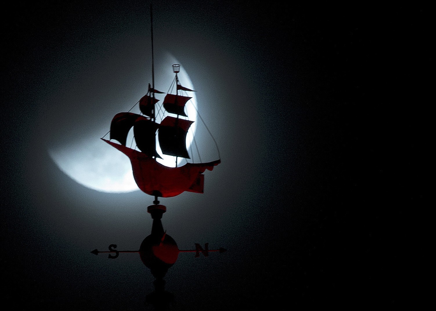 The Earth's shadow begins to fall over the moon during a total lunar eclipse, behind a weathervane shaped like a Spanish galleon on the Freedom Tower in Miami, Wednesday, Oct. 8, 2014.