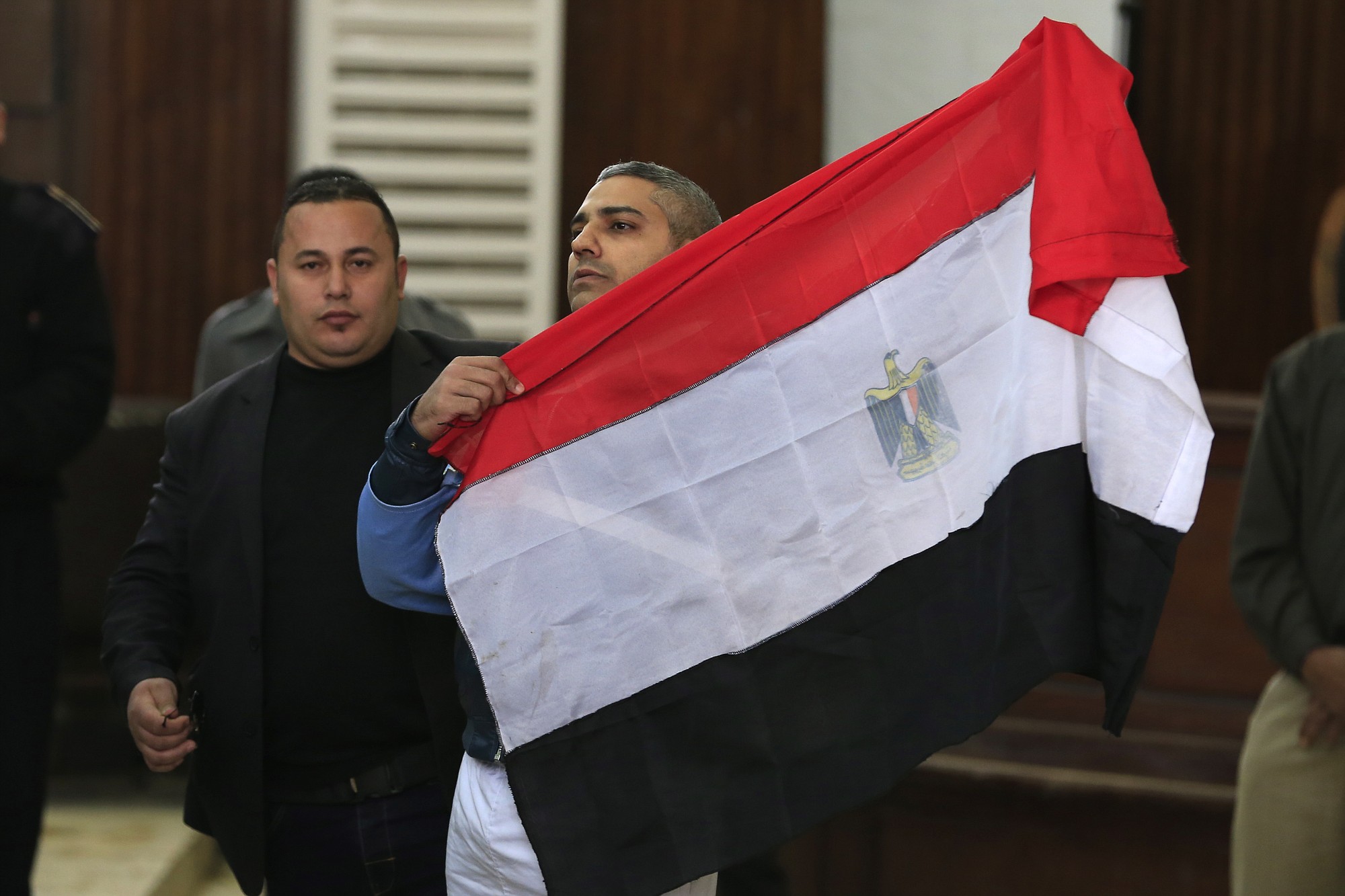 Journalist Mohamed Fahmy holds up an Egyptian flag Thursday at a courthouse near Tora prison in Cairo.