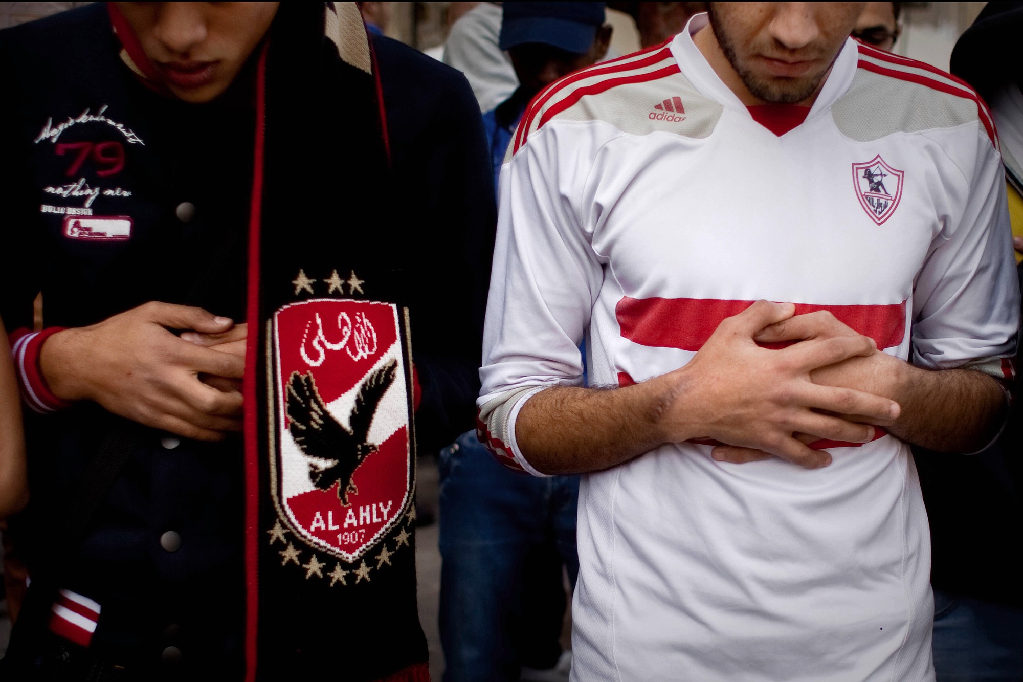 An Ultras Al-Ahly soccer fan, left, and an Ultras White Knights soccer fan, right, pray Monday for people who were killed on Sunday from a riot outside the Air Defense Stadium, at Cairo University in Egypt.