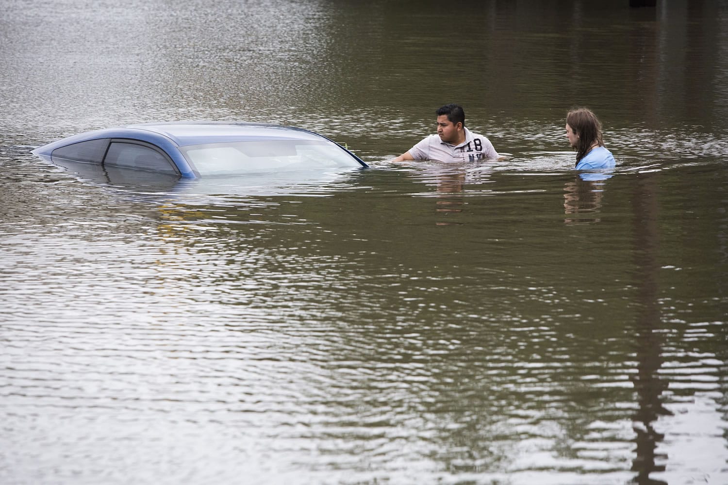Roberto Salas, left, and Lewis Sternhagen check a flooded car on a frontage road near the Willow Waterhole Bayou on Tuesday in Houston.