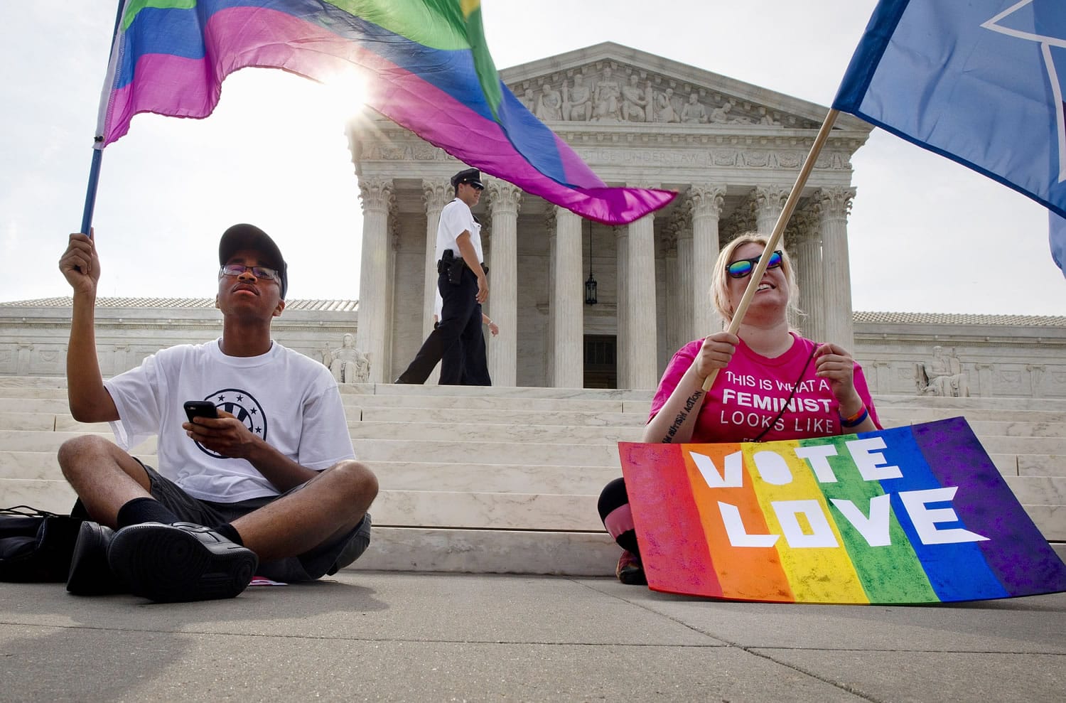 Carlos McKnight, 17, of Washington, left, and Katherine Nicole Struck, 25, of Frederick, Md., hold flags in support of gay marriage as security walks behind outside of the Supreme Court in Washington, Friday June 26, 2015.