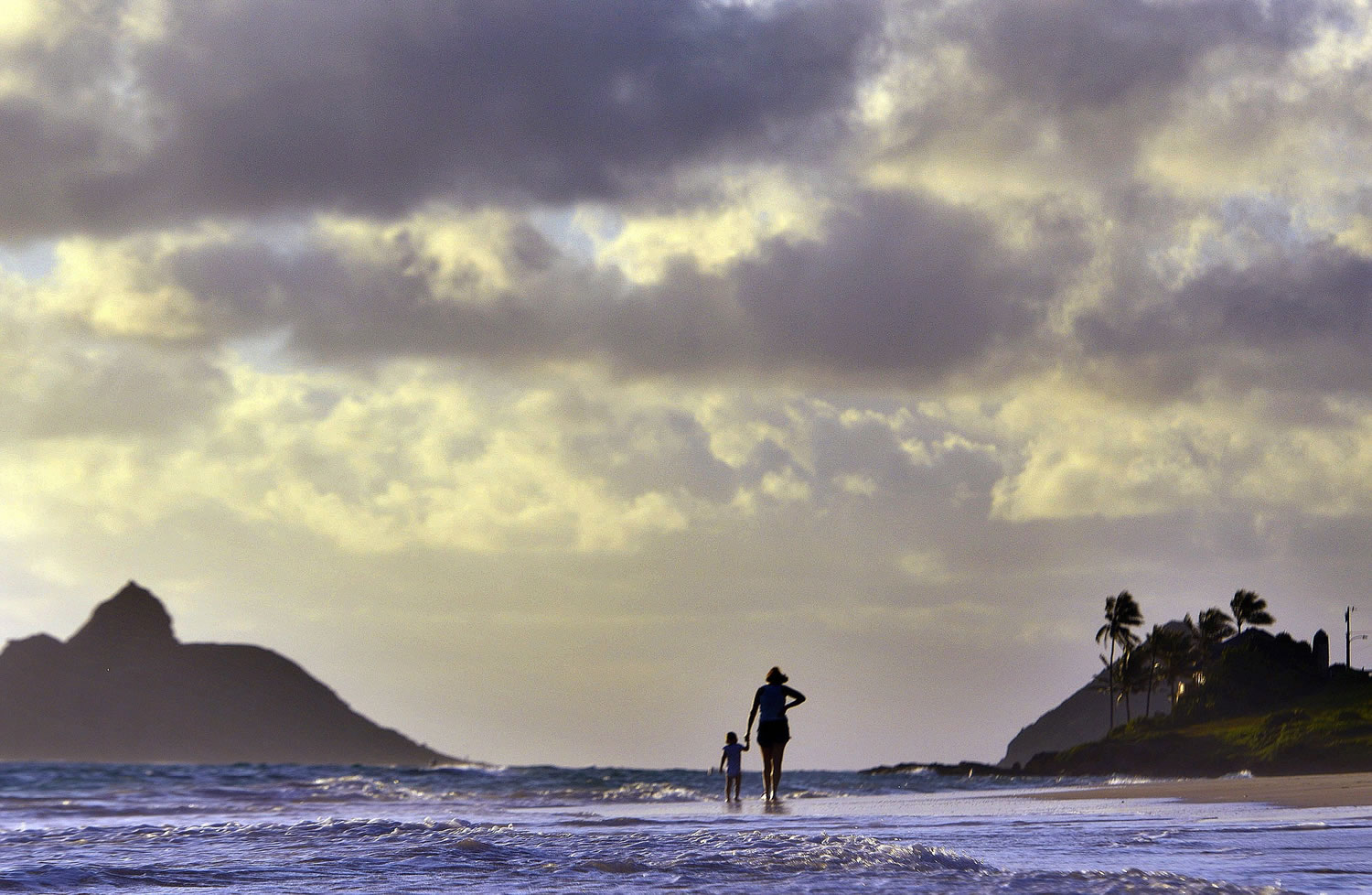 Anne Kllingshirn, of Kailua, Hawaii walks with her daughter Emma, 1, as storm clouds float overhead during the sunrise hours on Kailua Beach, in Kailua, Hawaii, on Thursday morning.