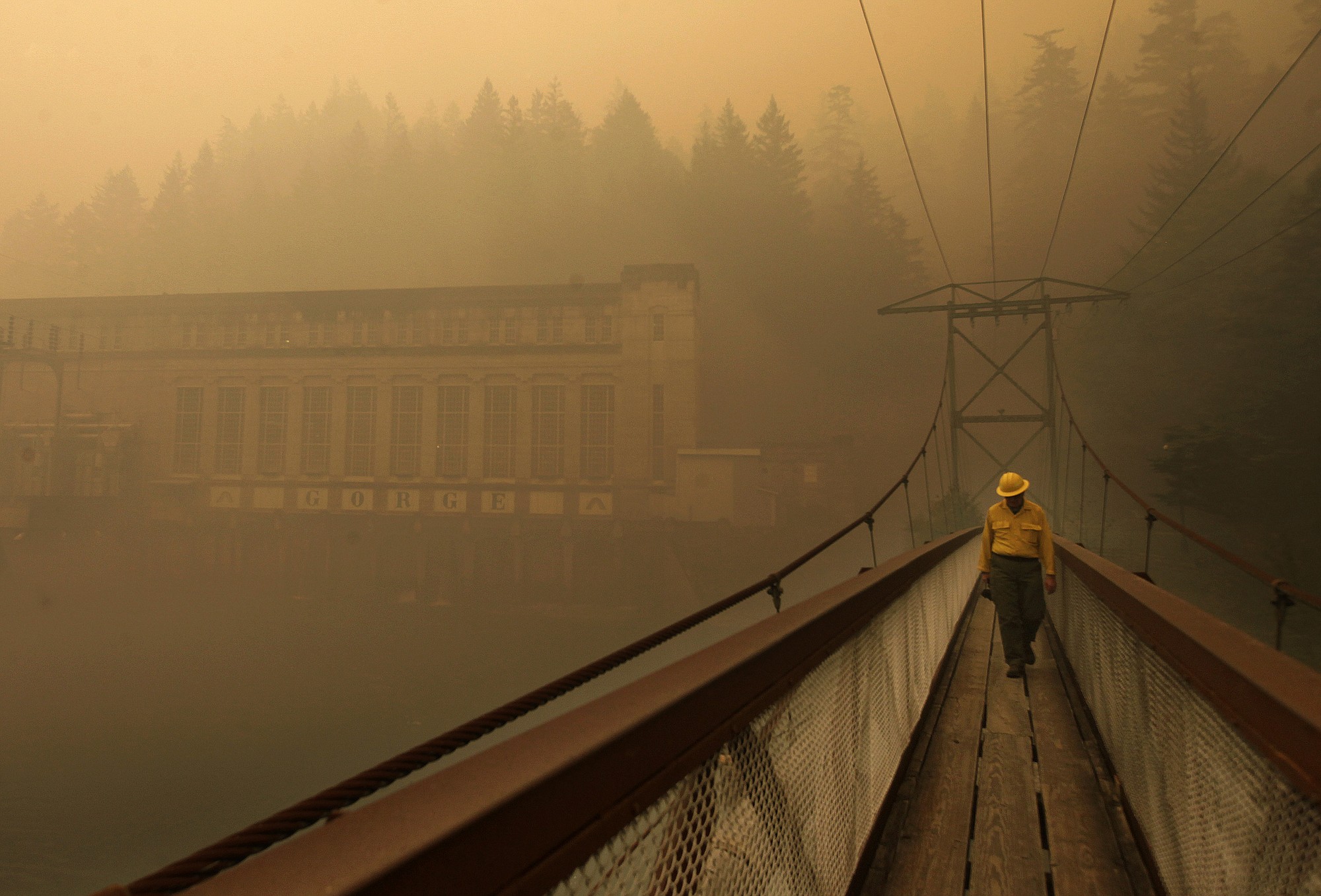Dennis Godfrey, with the Great Basin Incident Management Team 4, walks across a bridge from the Gorge Powerhouse, Wednesday, Aug. 26, 2015, near Newhalem, Wash. Smoky conditions grounded helicopters and airplanes Wednesday that had been fighting the fires.