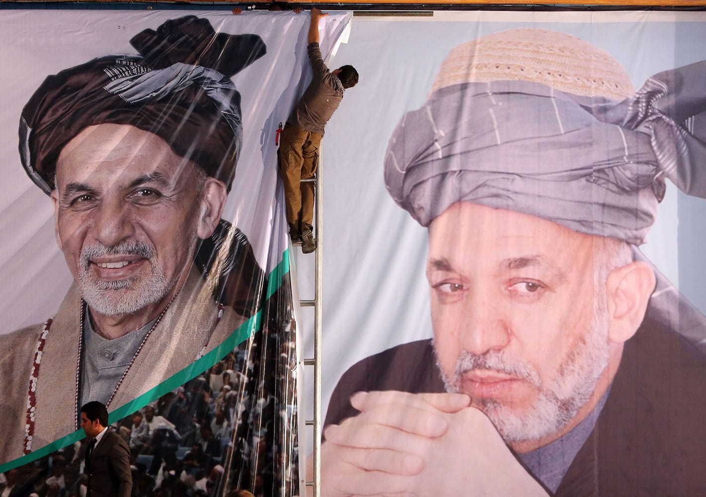 An Afghan boy prepares a banner of Afghan president-elect, Ashraf Ghani Ahmadzai, next to a banner of outgoing President Hamid Karzai during his first public appearance since winning the election runoff in Kabul, Afghanistan, on Monday.