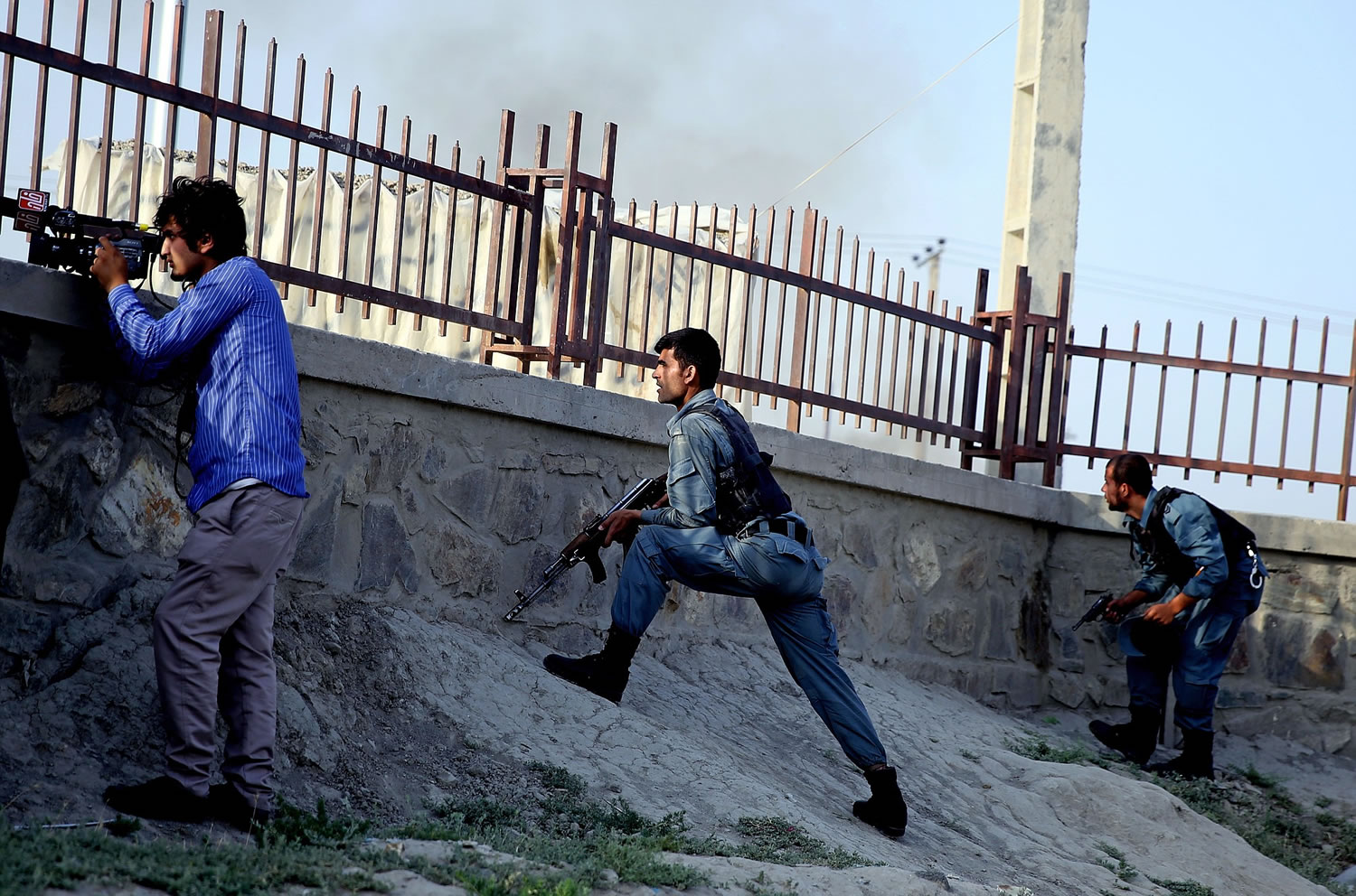 Afghan security forces and a journalist take cover during clashes with Taliban fighters in Kabul, Afghanistan, Thursday, July 17, 2014. Gunmen launched a pre-dawn attack on the Kabul International Airport in the Afghan capital on Thursday, raining down rockets, setting off a gunbattle with security forces and forcing the airport to close for hours, officials said. The militants occupied two buildings which were under construction some 700 meters (yards) north of the facility, and were using them as a base to direct rockets and gunfire toward the airport and international jet fighters flying over Kabul, said Afghan army Gen. Afzal Aman.