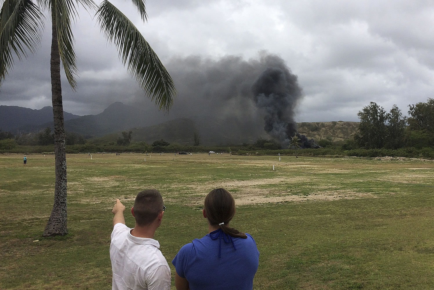 A man and woman look toward smoke rising from a Marine Corps Osprey aircraft after making a hard landing on Bellows Air Force Station near Waimanalo, Hawaii.