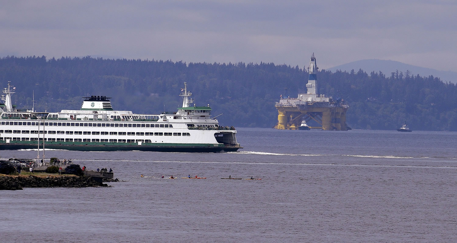 A Washington state ferry sails in view of the oil drilling rig Polar Pioneer and a handful of kayakers while being towed toward a dock Thursday, May 14, 2015, in Seattle. The rig is the first of two drilling rigs Royal Dutch Shell is outfitting for oil exploration and was towed to the Port of Seattle site despite the city's warning that it lacks permits and threats by kayaking environmentalists to paddle out in protest.